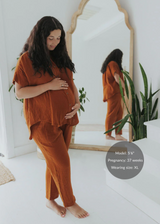 Pregnant woman in a rust-colored Everyday Breeze Pant and matching top made of textured cotton gauze.