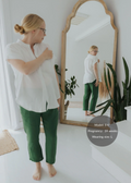 Woman in a white cotton gauze shirt and green Everyday Breeze Pant, reflected in a mirror.