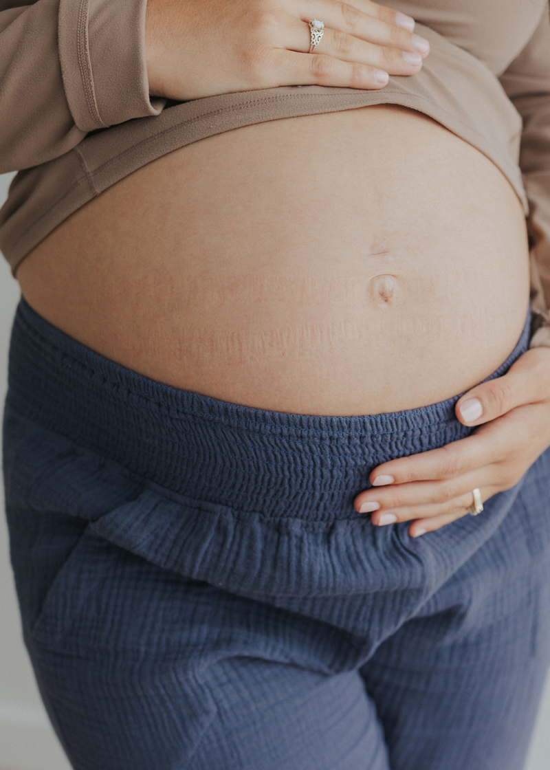 Pregnant belly wearing Everyday Breeze Pant in blue cotton gauze with elastic waistband.
