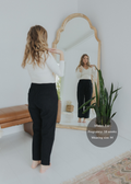Woman in black smocked linen maternity pants and white top, reflected in a mirror.