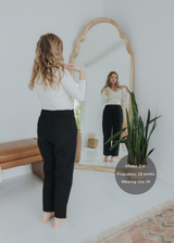 Woman in black smocked linen maternity pants and white top, reflected in a mirror.