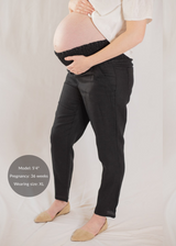 Pregnant model in black smocked linen maternity pants with functional pockets and tan flats.