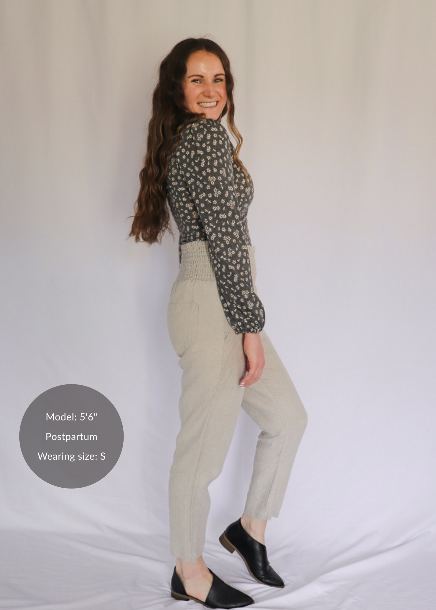 Smiling woman in smocked beige linen pants, black flats, and a floral top.