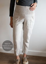 Pregnant model wearing natural linen smocked maternity pants with pockets and rolled cuffs.