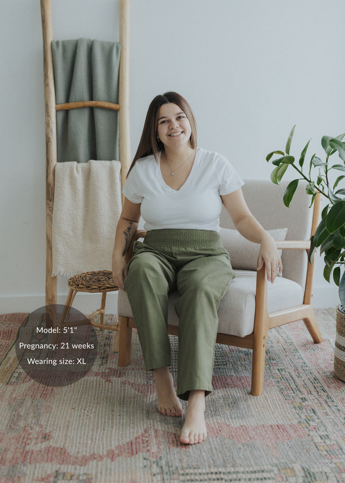 Smiling woman in olive green smocked linen pants and white tee, seated.