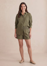 Smiling woman in a relaxed-fit olive green cotton gauze shirt and matching smocked-waist shorts.