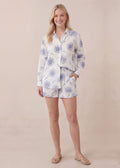 Blonde woman in white cotton gauze set with blue floral print, long-sleeve top, and matching shorts.