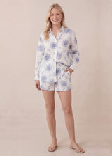 Blonde woman in white cotton gauze set with blue floral print, long-sleeve top, and matching shorts.