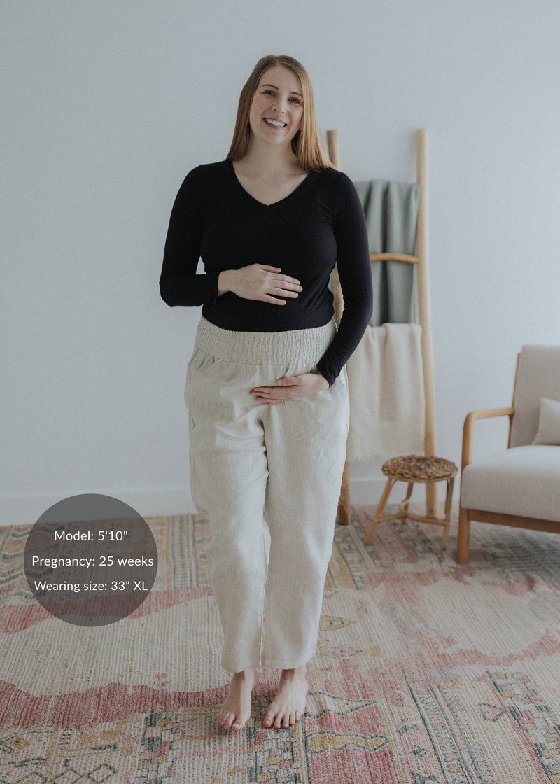 Smiling pregnant woman in natural linen smocked maternity pants with extended inseam and black top.