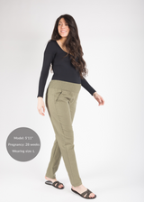 Smiling pregnant woman in olive green linen maternity pants with smocked waistband and black long-sleeve top.