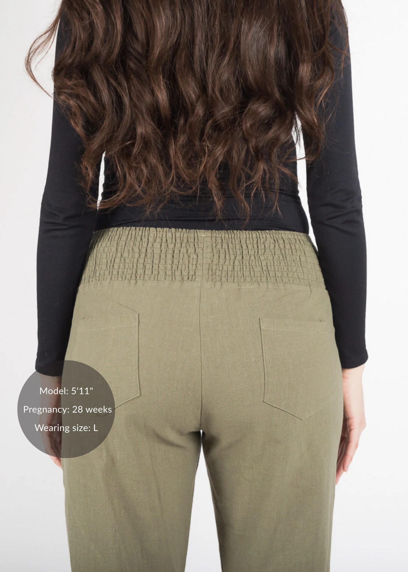 Back view of a pregnant model wearing olive green linen maternity pants with a smocked waistband.