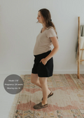 Pregnant woman in black smocked cotton/linen shorts with pockets and a beige top.
