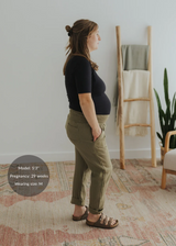 Pregnant woman in olive green cotton gauze Everyday Breeze Pant with elastic waistband and pockets.