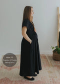 Woman in black cotton poplin waist-gathered dress, side view, 17.5 weeks pregnant, wearing size S.
