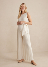 Smiling woman in a white pleated Tencel jumpsuit with a waist tie and wide legs.