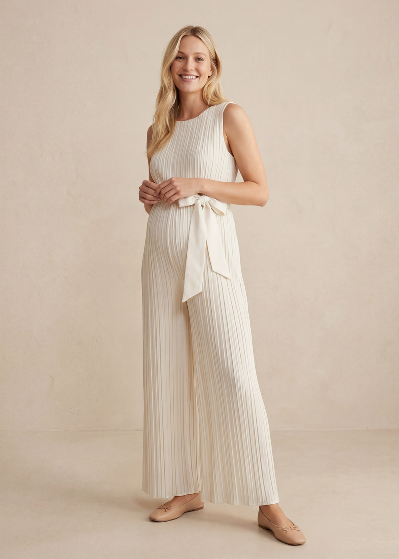 Smiling woman in a white pleated Tencel jumpsuit with a waist tie and wide legs.