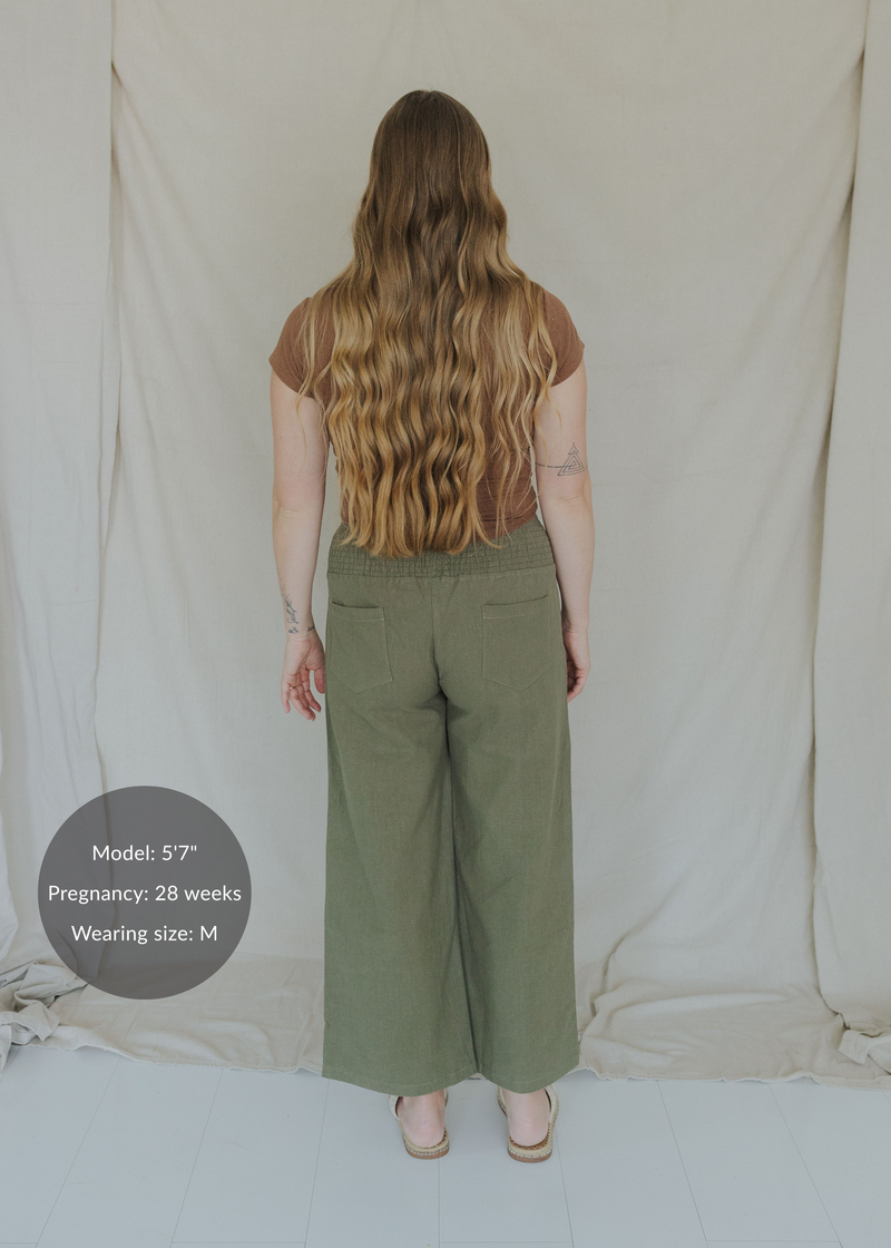 Back view of a pregnant model in olive green wide-leg linen pants with a smocked waistband.
