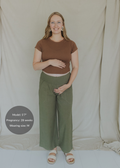 Smiling pregnant woman in olive wide-leg linen pants with a smocked waistband and a brown top.