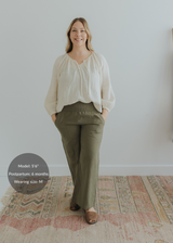 Smiling woman in olive green wide-leg linen pants with smocked waistband and cream blouse.