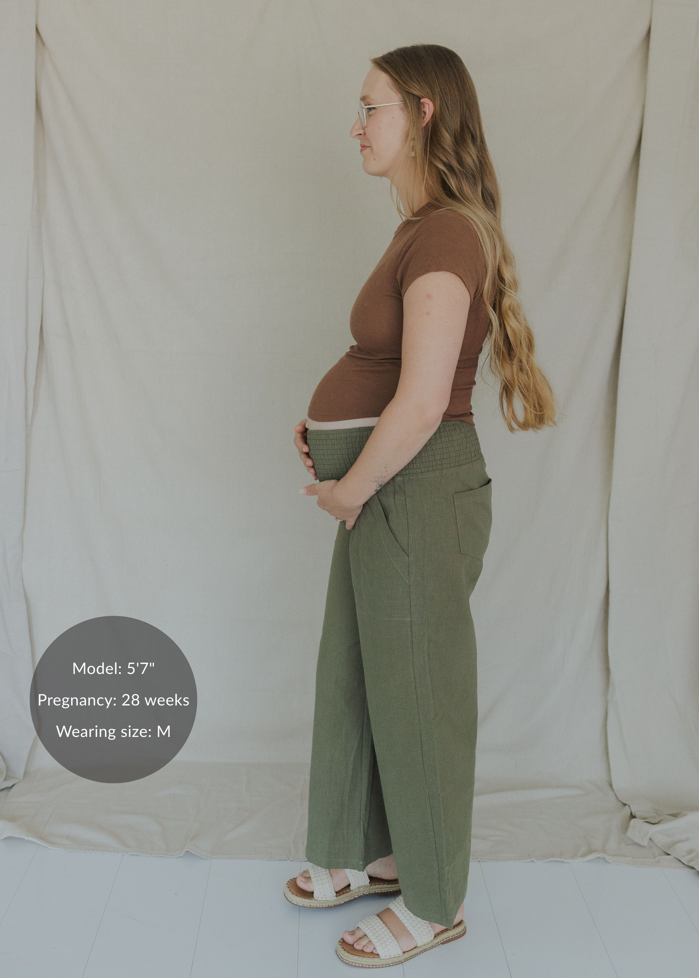 Pregnant woman in olive green wide-leg smocked linen pants and a brown top.