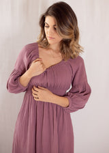 Woman in a plum Eliza Maternity and Nursing Dress, featuring a smocked bodice, balloon sleeves, and cotton gauze fabric.