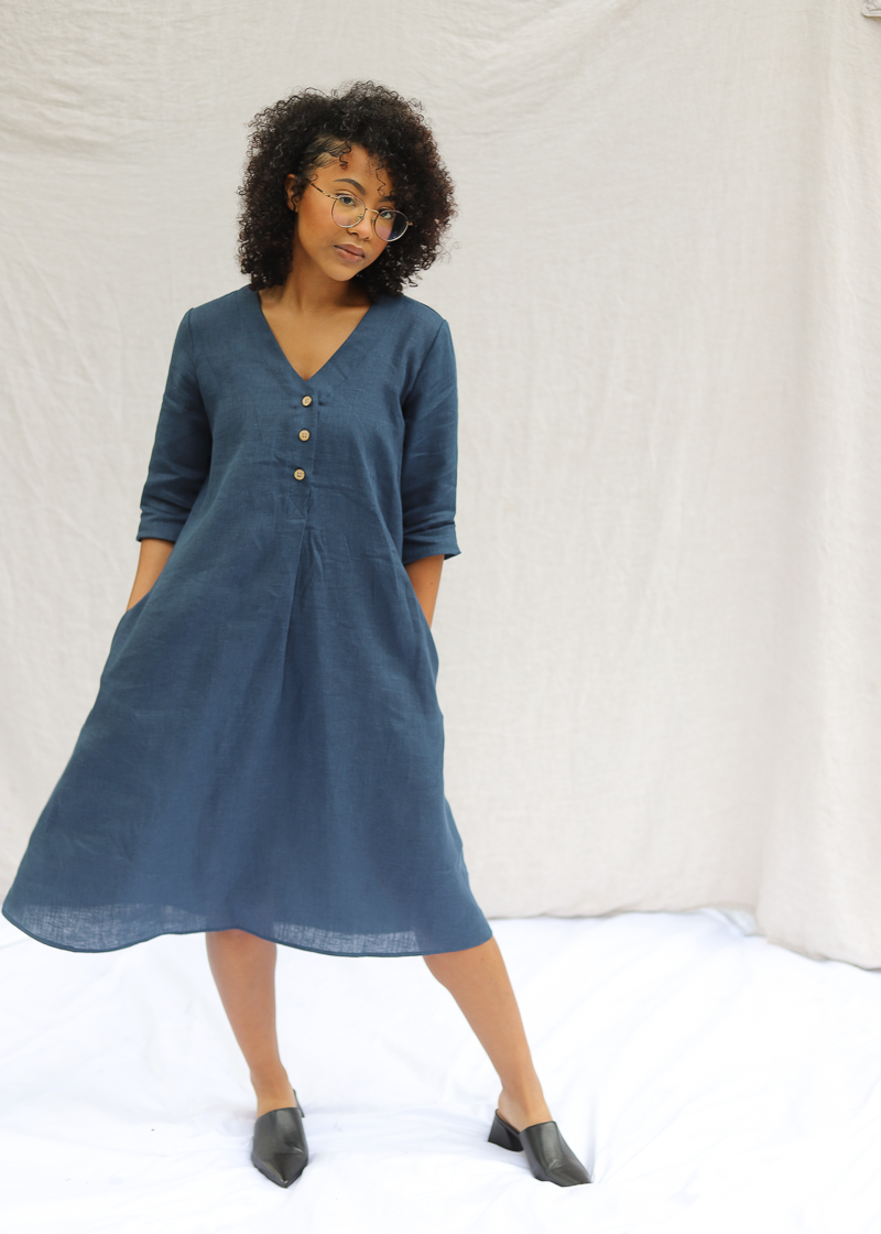 Woman wearing the Faye Dress in pacific blue softened linen, with front buttons and a waist tie.