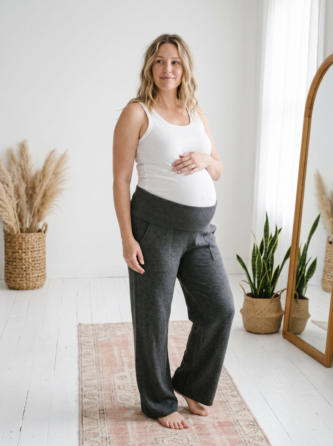 Pregnant model wearing heather charcoal grey knit cotton viscose maternity sweater pants and a white ribbed tank top.