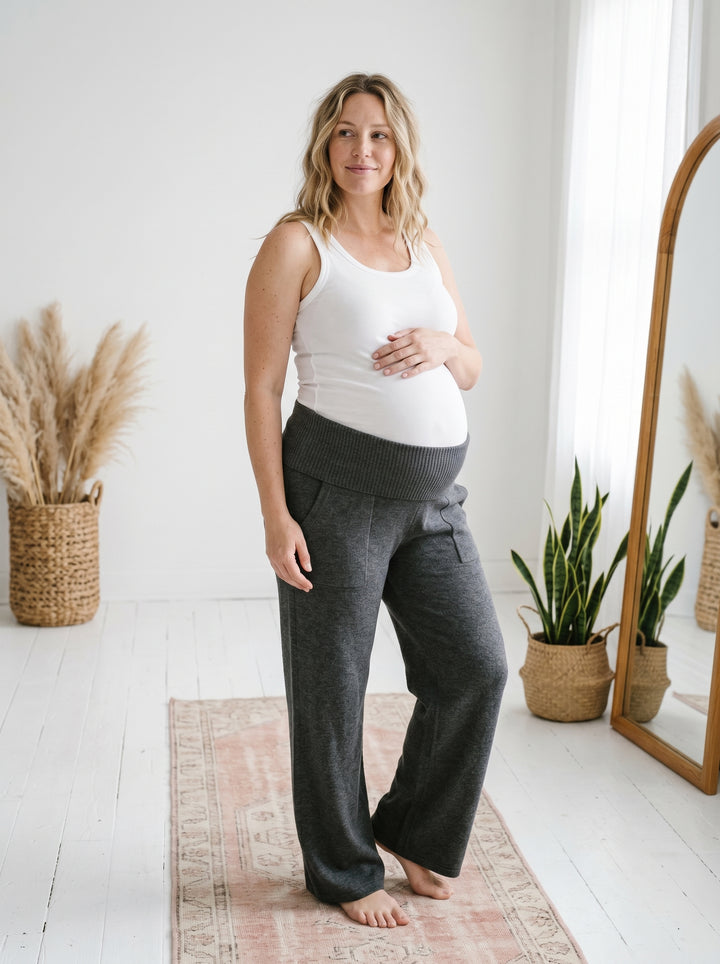 Pregnant model wearing heather charcoal grey knit cotton viscose maternity sweater pants and a white ribbed tank top.