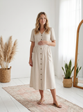 Pregnant woman in a beige linen-cotton button-front nursing dress with V-neck, short puffed sleeves, and patch pockets.