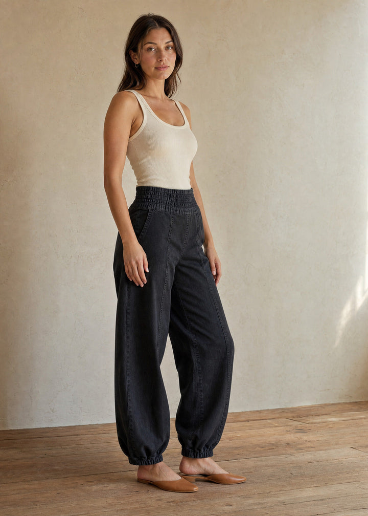 Woman wearing the Balloon Jean Pant in black with a cream tank, full length in warm indoor light