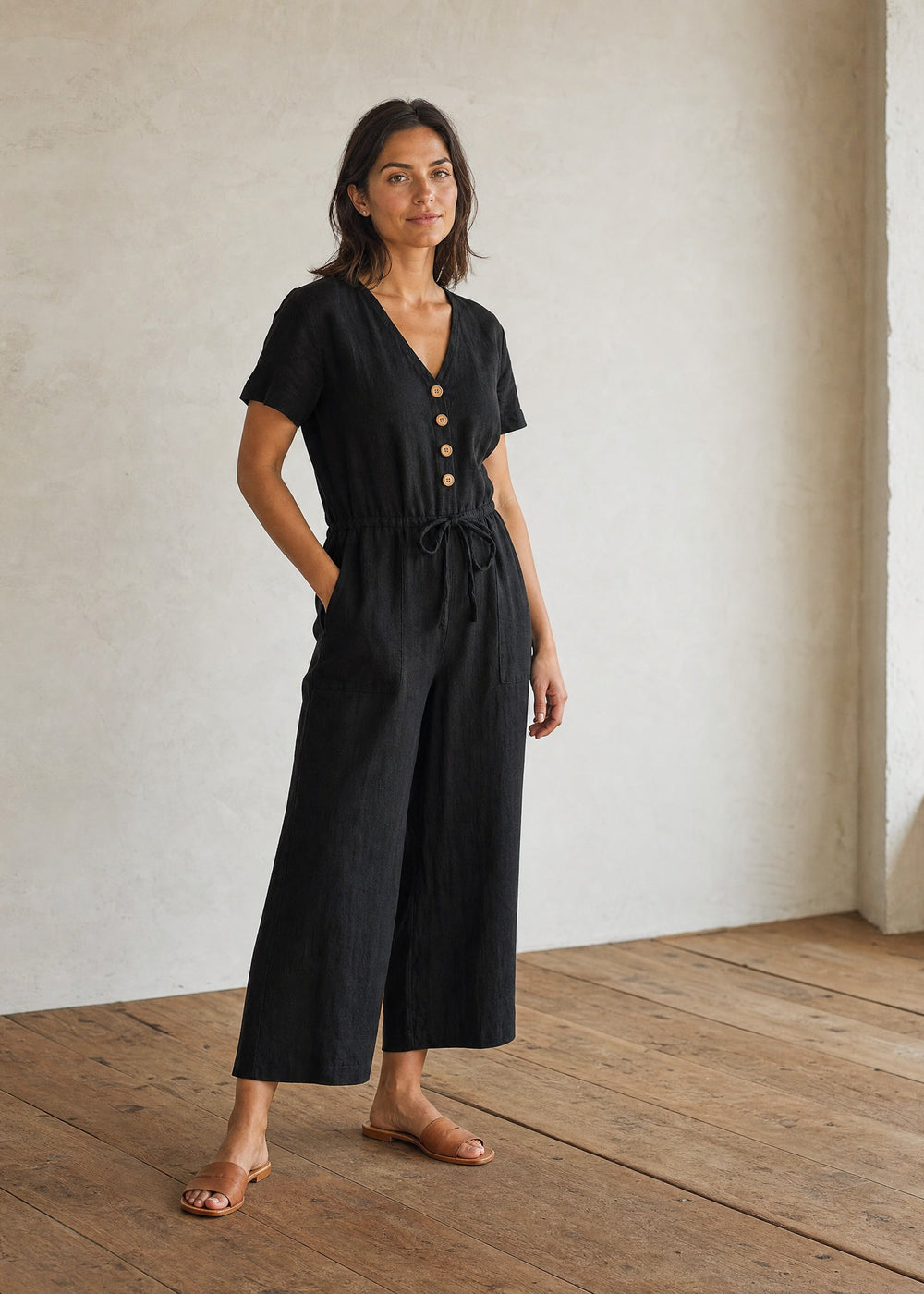 Woman wearing the Easy On/Off Jumpsuit in black linen, full length in warm indoor light