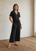 Woman wearing the Easy On/Off Jumpsuit in black linen, full length in warm indoor light